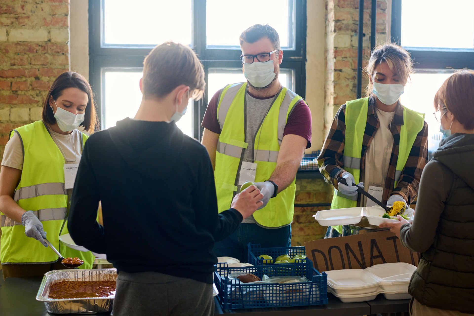 Three volunteers in protective masks passing food to refugees in camp